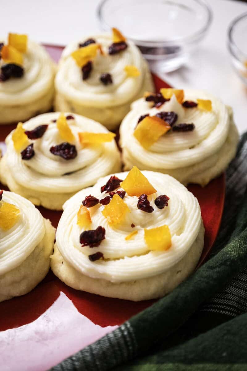 Cranberry and orange shortbread cookies topped with frosting and garnished with dried cranberries and candied oranges.