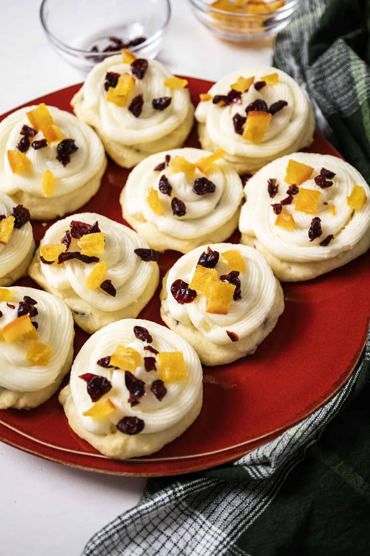 Cranberry and orange shortbread cookies topped with frosting and garnished with dried cranberries and candied oranges.