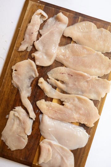 Thinly sliced chicken breast laid out on cutting board.