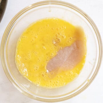 Chicken cutlet dipped in egg in bowl.