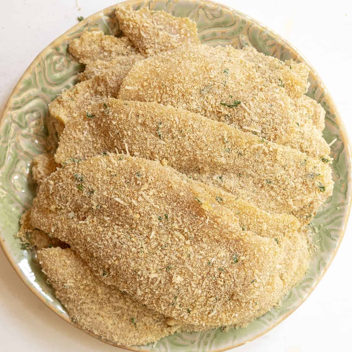 Chicken breast dredged in breadcrumbs piled on a plate.