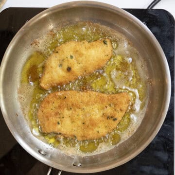 Chicken cutlets frying in oil and flipped over.