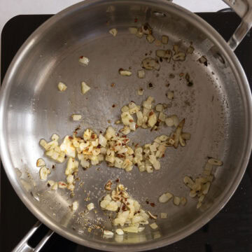 Garlic and shallots sauteing in a pan with seasoning.