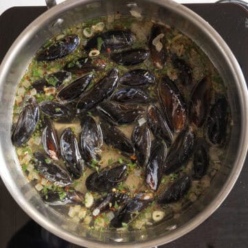Mussels in a pan of simmering white wine.