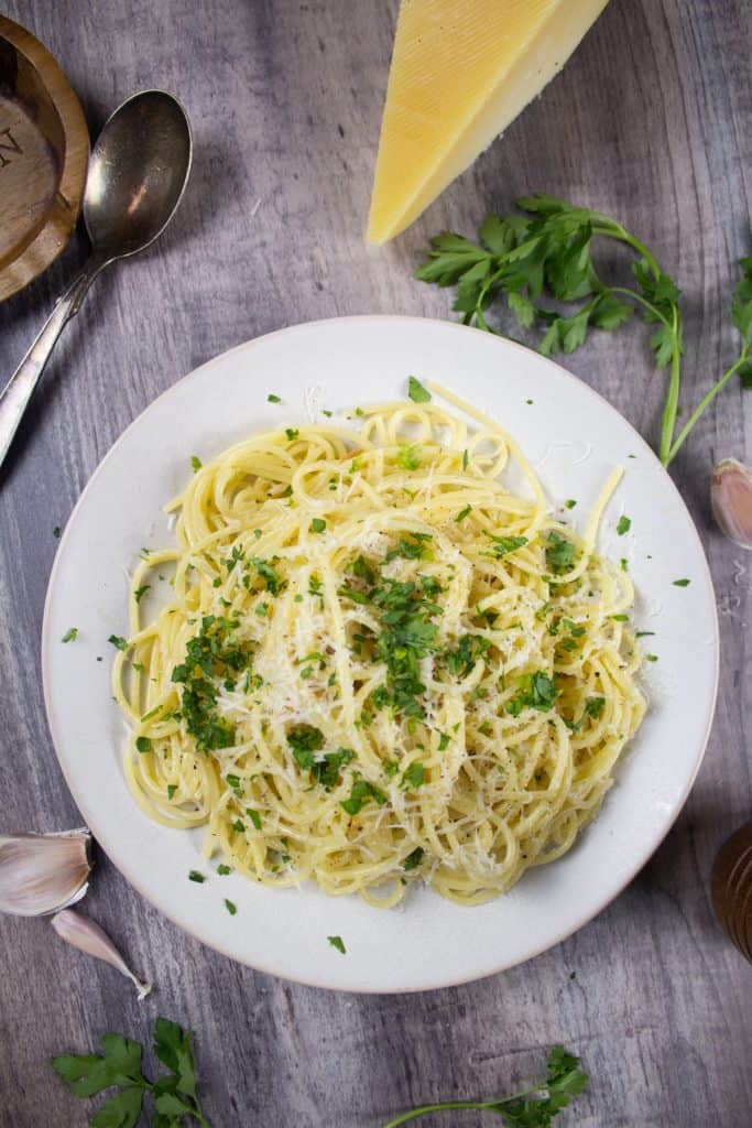 spaghetti with garlic and oil with garlic cloves, parsley and parmesan in frame