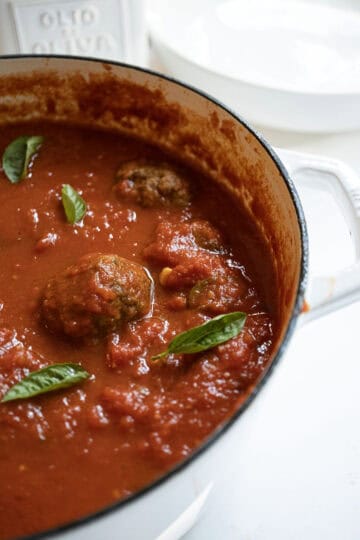 A pot filled with sauce and meatballs, garnished with basil.