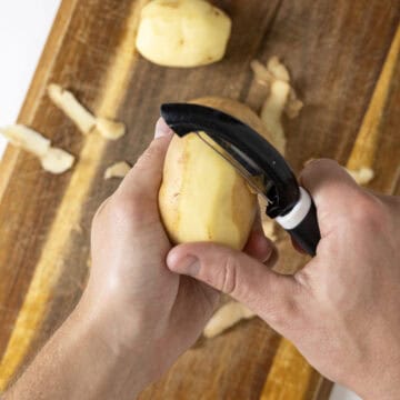 Peeling potatoes over cutting board.