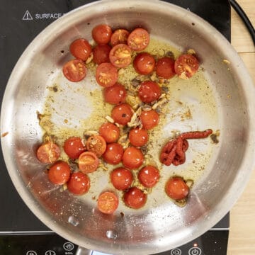 Cherry tomatoes breaking down with garlic in a pan.