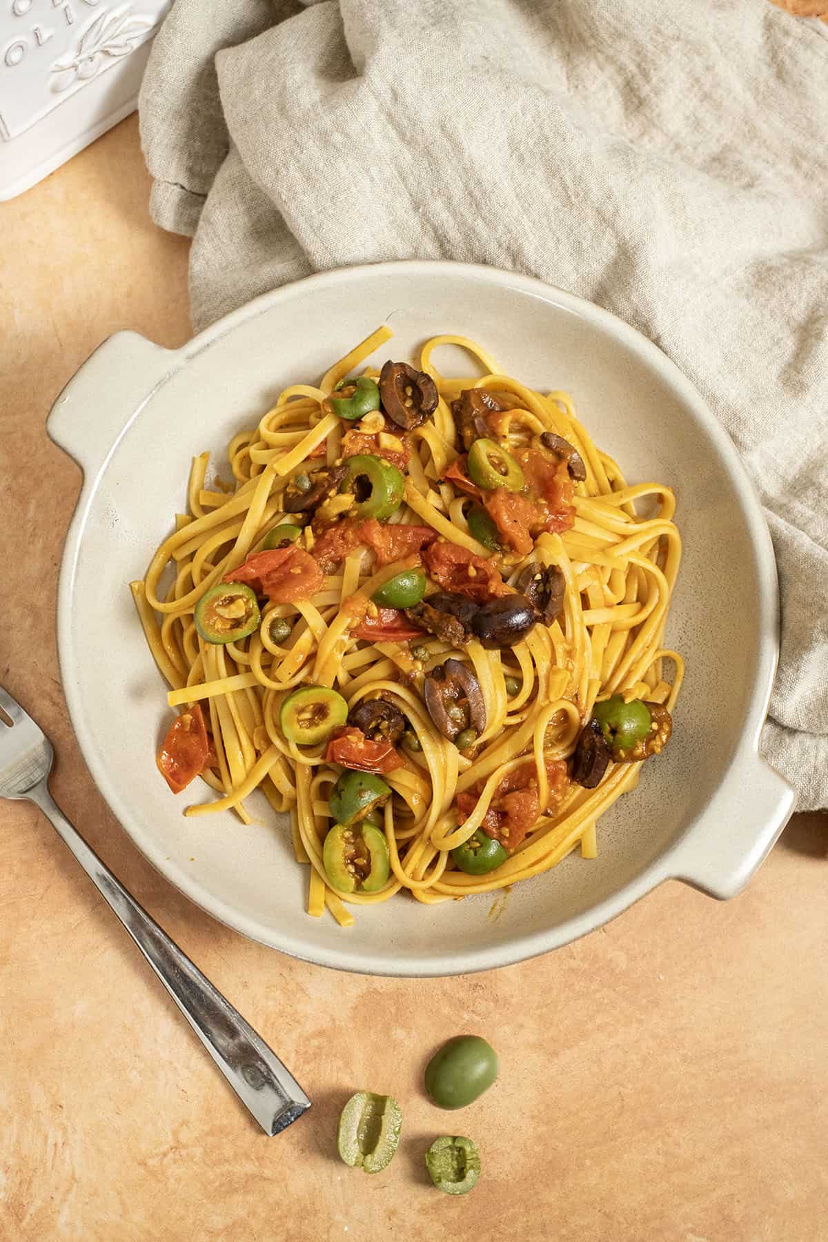 Linguine puttanesca topped with olives and capers in a bowl.