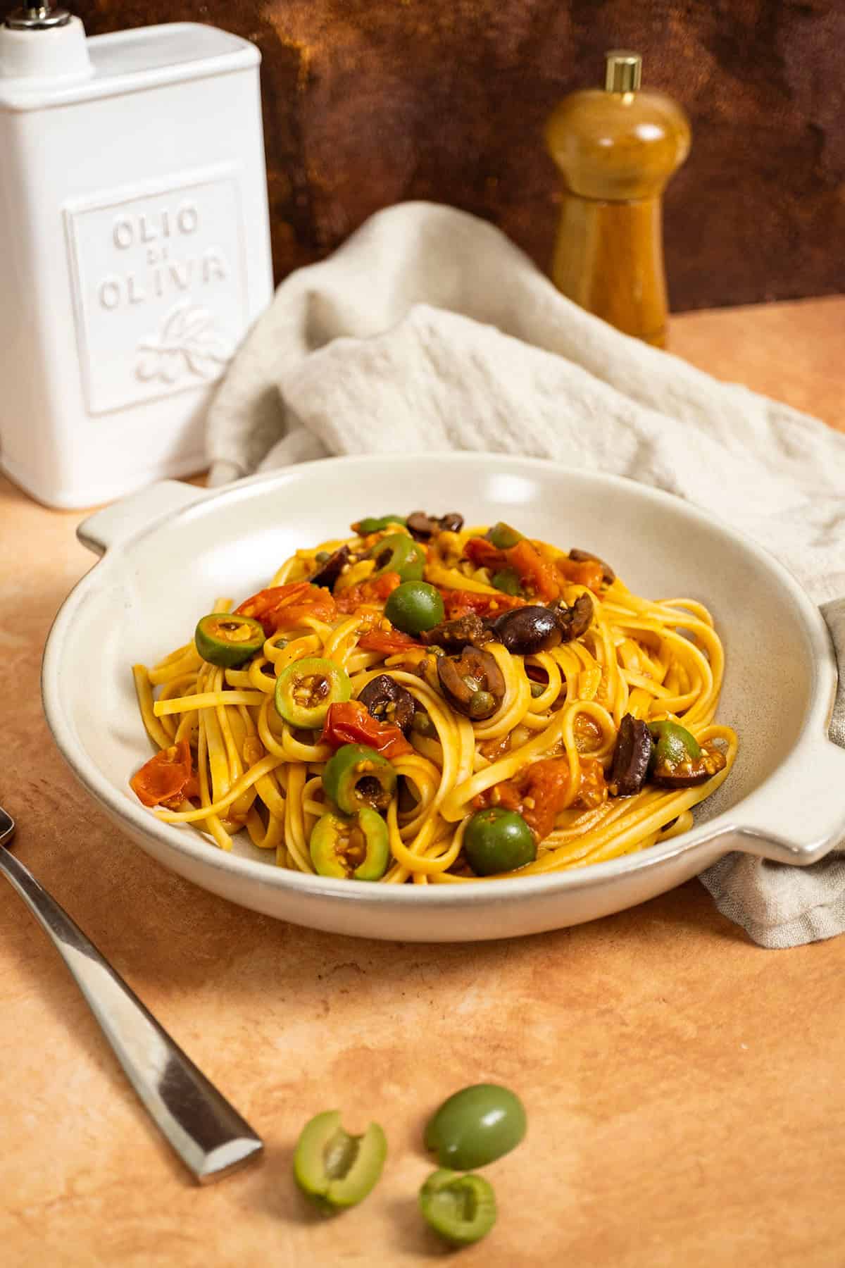Linguine puttanesca topped with olives and capers in a bowl.