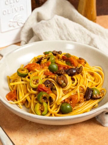 Linguine puttanesca topped with olives and capers in a bowl.