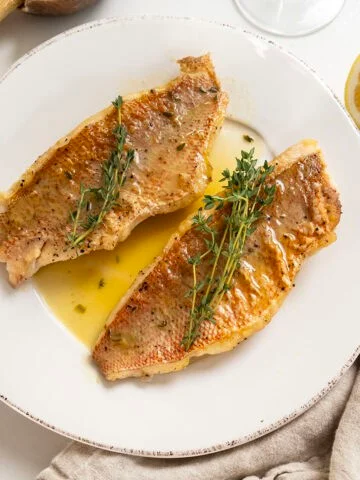 2 filets of pan seared vermillion snapper on a plate garnished with thyme sprigs.