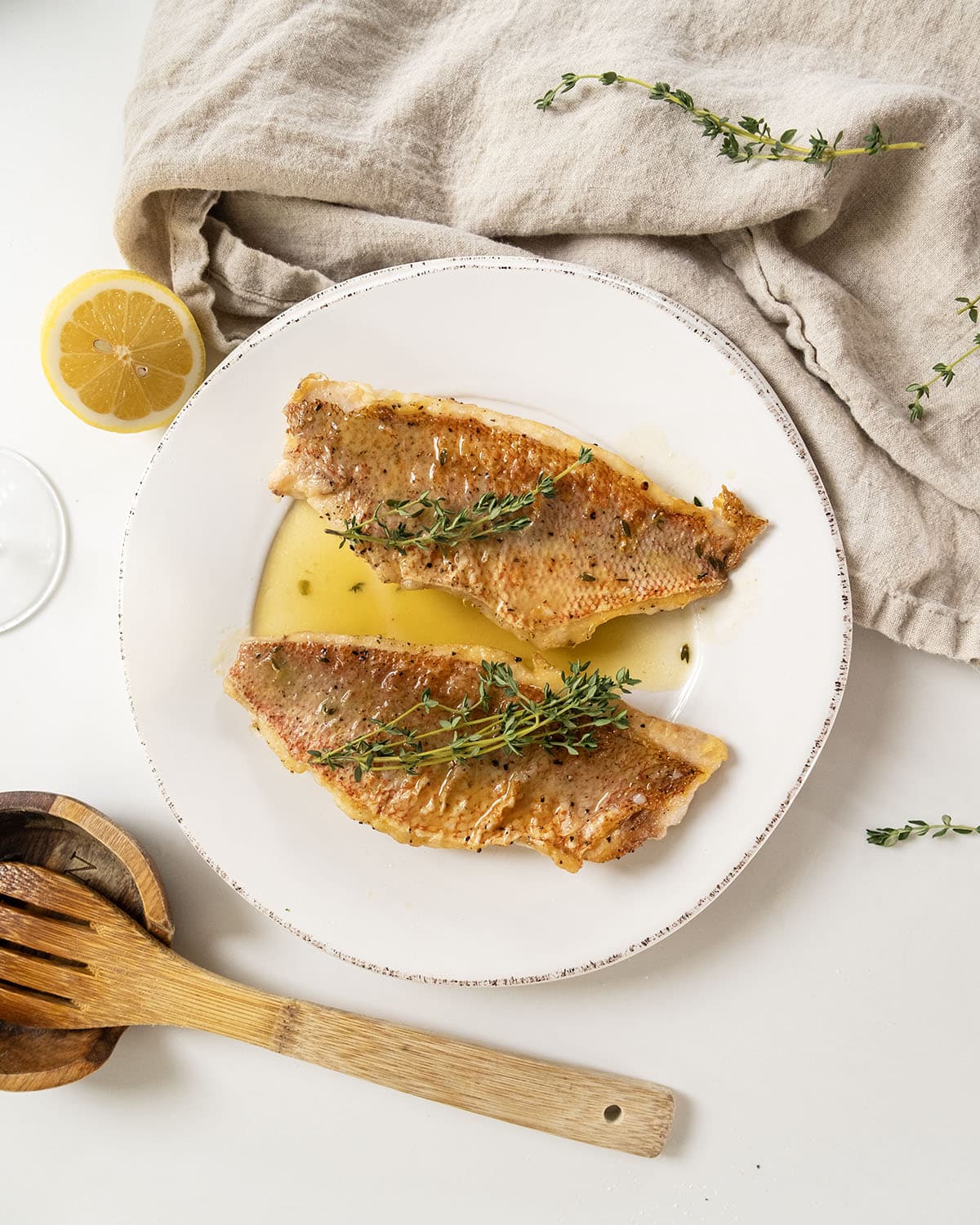 2 filets of pan seared vermillion snapper on a plate garnished with thyme sprigs.