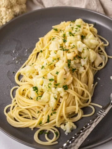 spaghetti with cauliflower plated on a dish garnished with parsley.