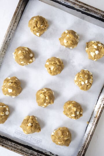 Cookies rolled into balls on a parchment paper lined baking sheet.