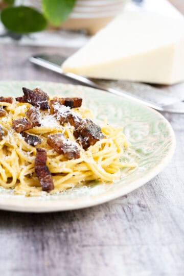 Finished spaghetti carbonara on a plate topped with extra pecorino.
