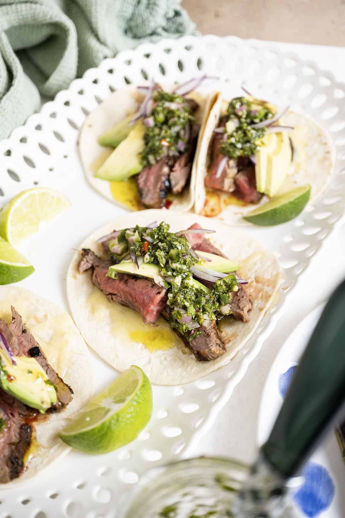 Chimichurri steak tacos on a plate with limes.