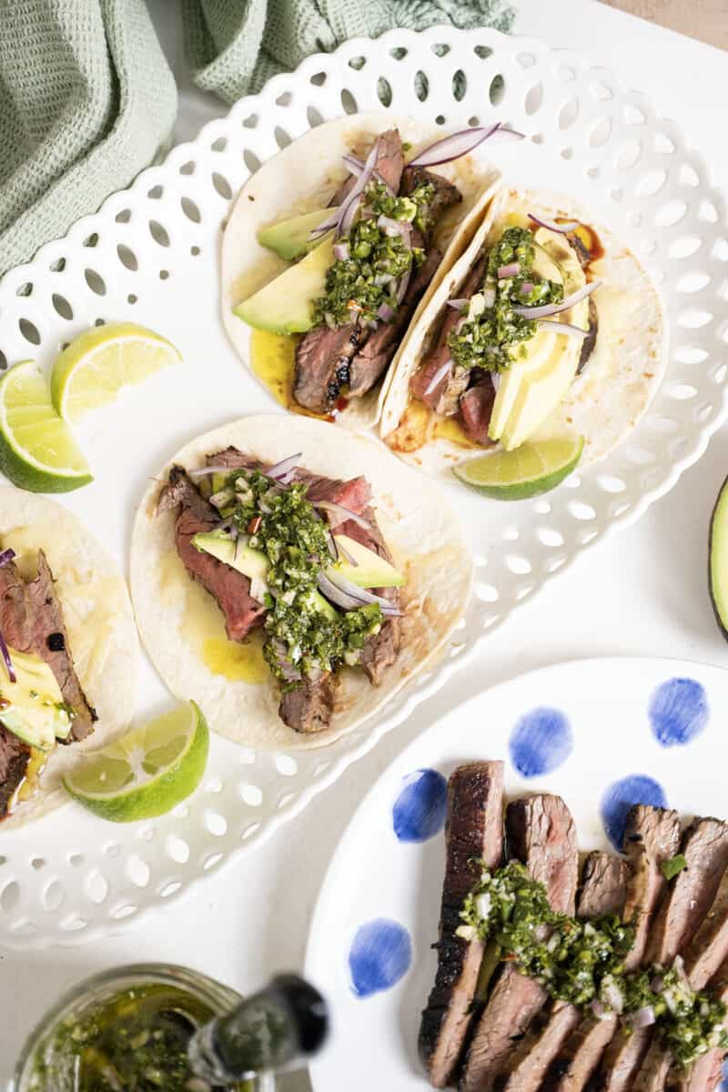 Chimichurri steak tacos on a plate with limes.