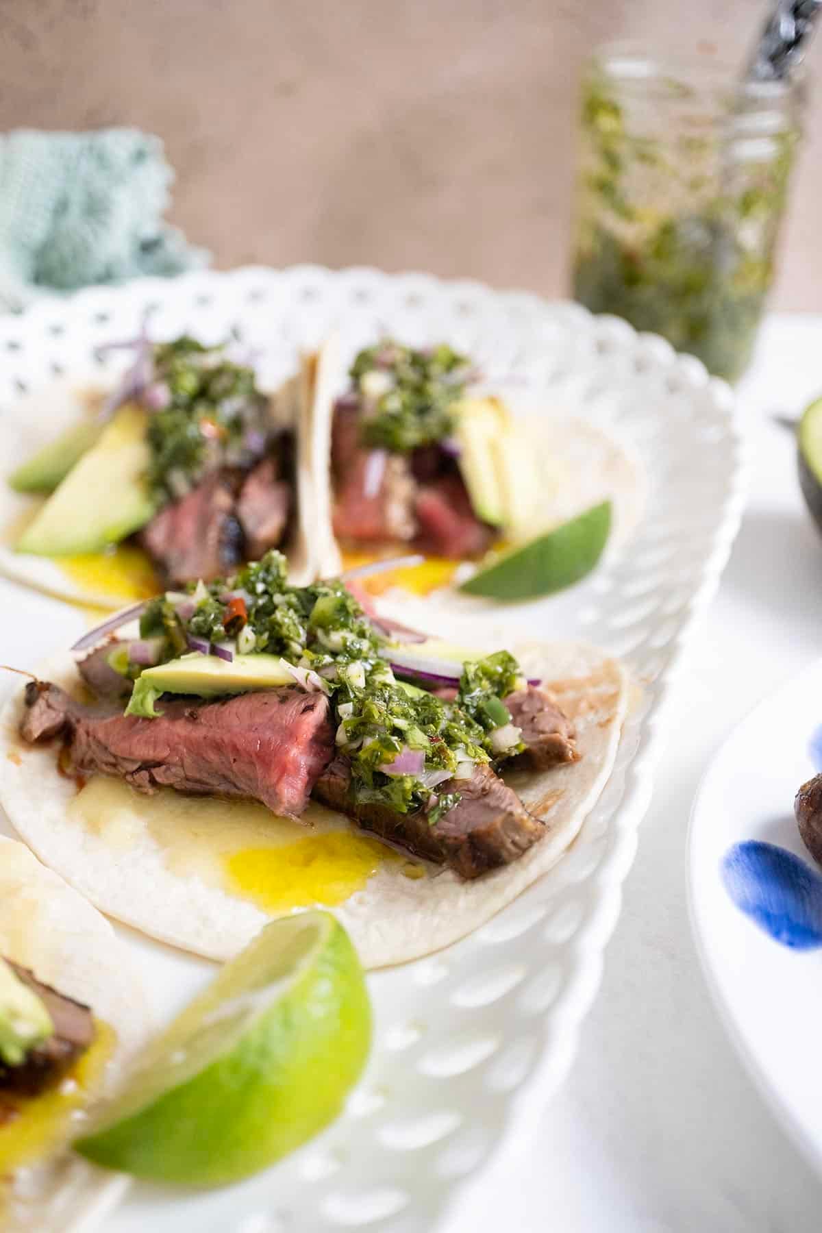 Chimichurri steak tacos on a plate with limes.