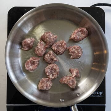 Pieces of ground sausage searing on a pan.