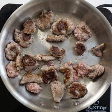 Pieces of ground sausage searing on a pan.