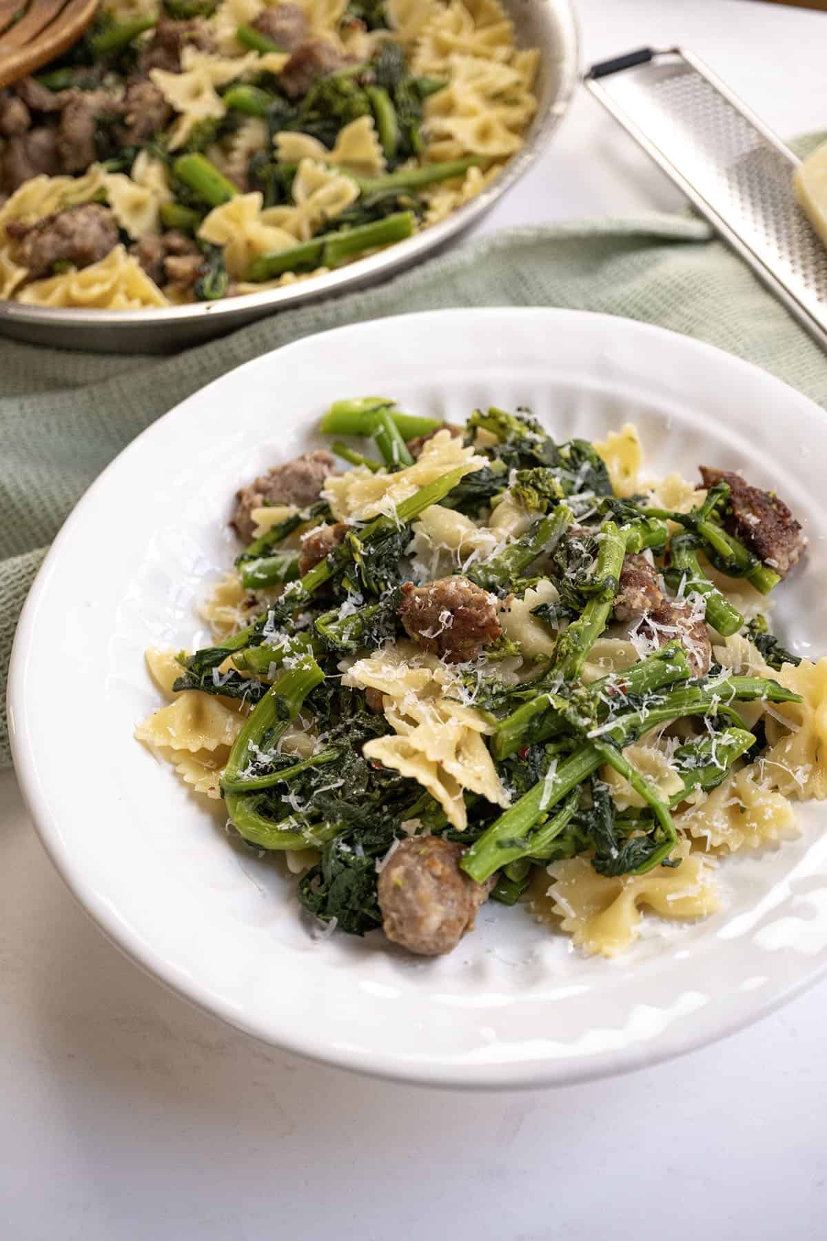 Farfalle with sausage and broccoli rabe, topped with parmesan on a plate.
