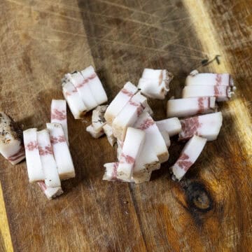 Chopped guanciale in strips on a cutting board.