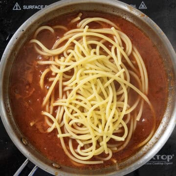 Bucatini pasta added to sauce in saucepan.
