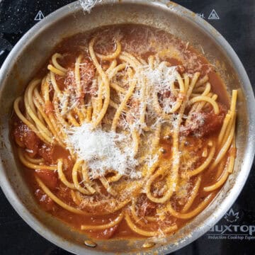 Bucatini combined with sauce and topped with pecorino in sauce pan.
