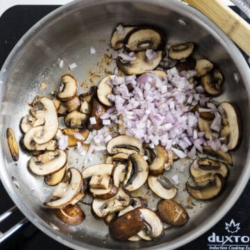 Frying mushrooms in the pan that are slightly browned with fresh chopped shallots just added.