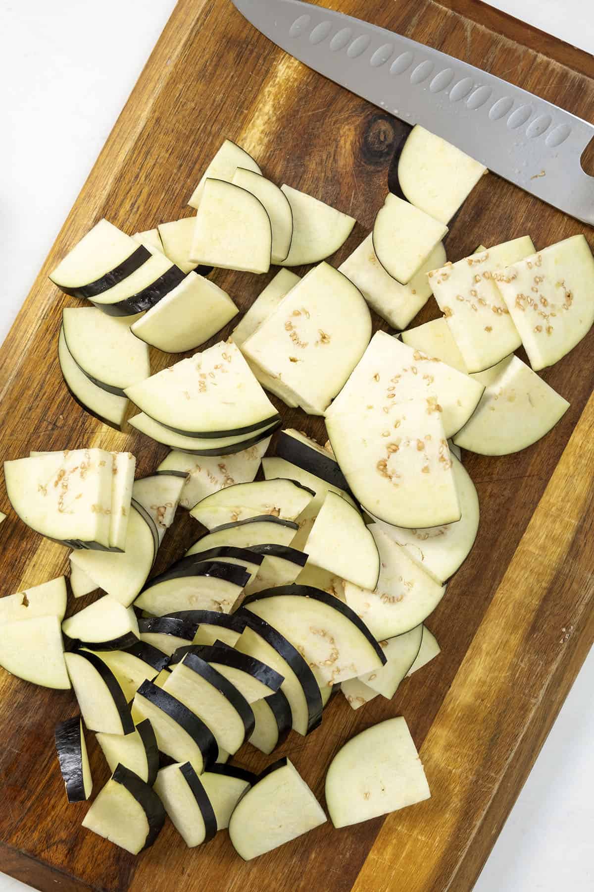 Eggplant sliced thin and cut into quarters, lying on a cutting board.