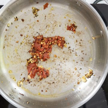 Tomato paste caramelizing in the saucepan with garlic and seasonings.