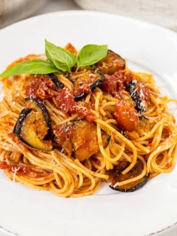 Pasta alla norma plated on a dish and garnished with basil.