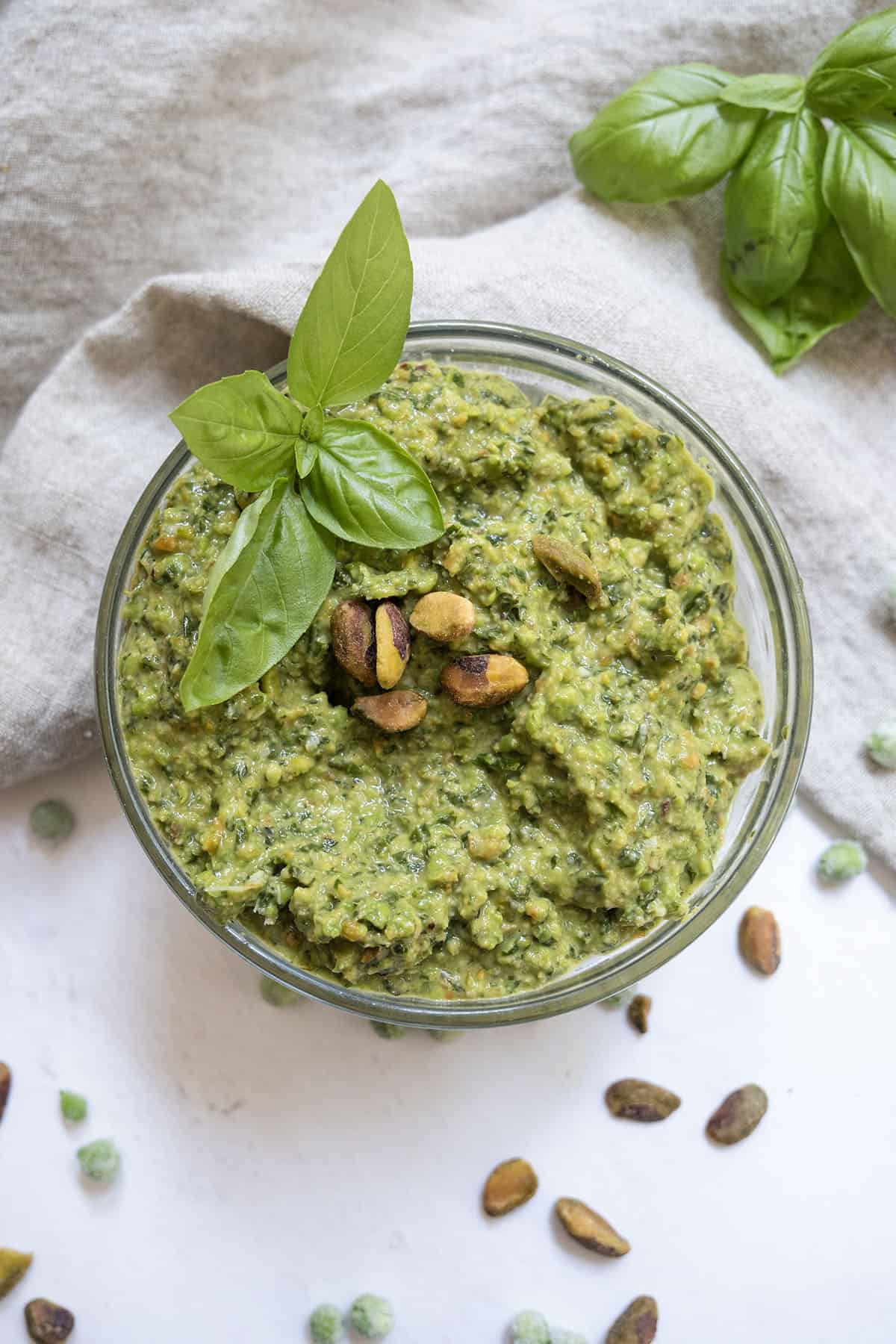 Pea pesto topped with pistachios and basil in a small bowl.