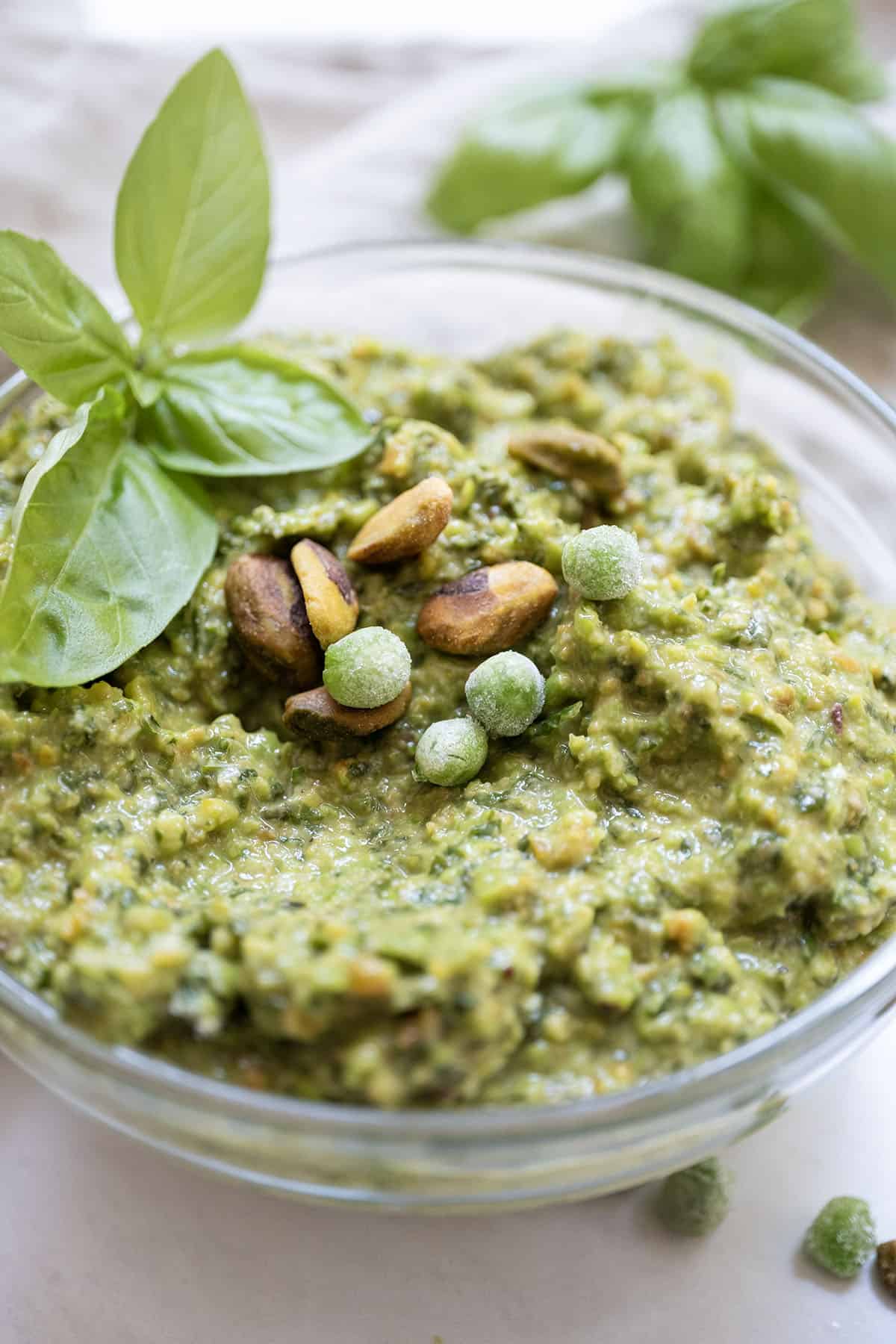 Pea pesto topped with pistachios and basil in a small bowl.