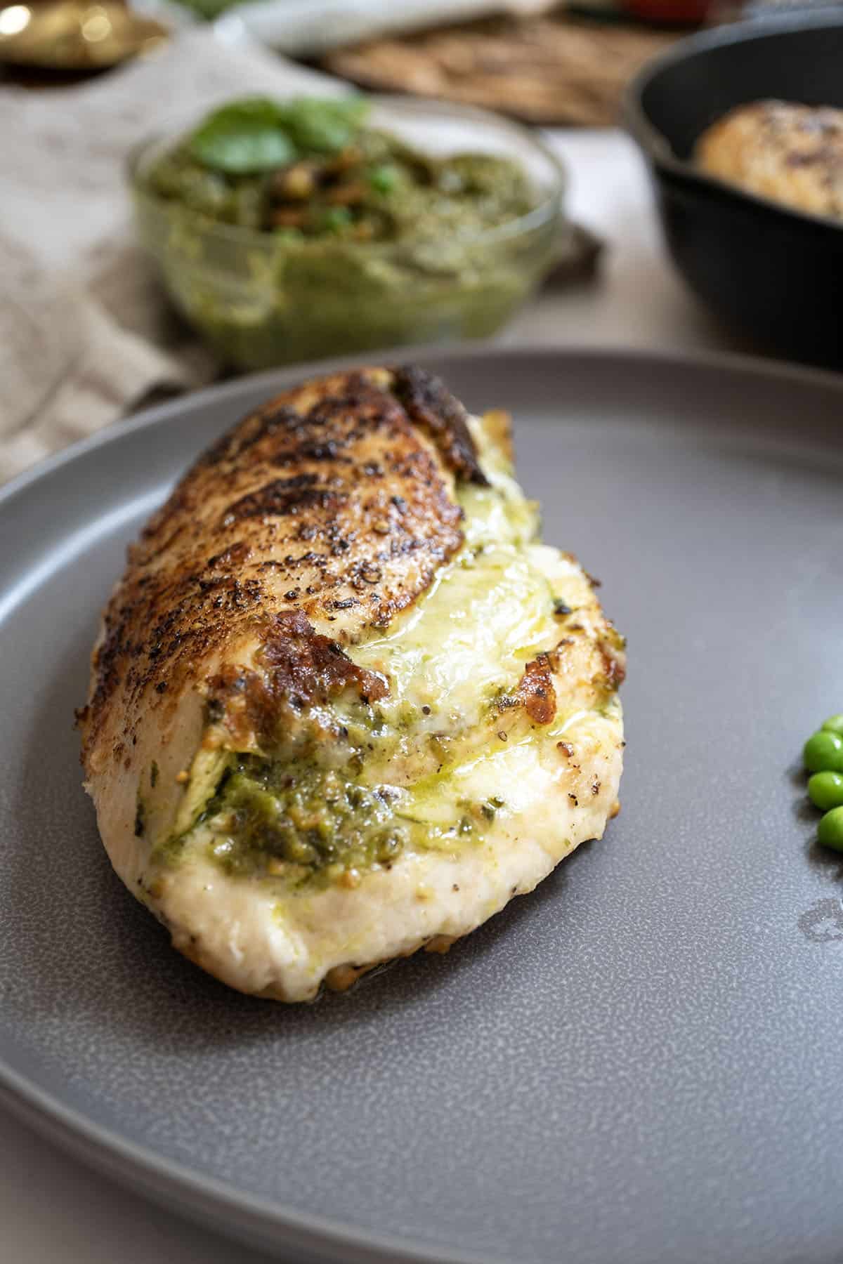 Pesto stuffed chicken on a plate with peas.