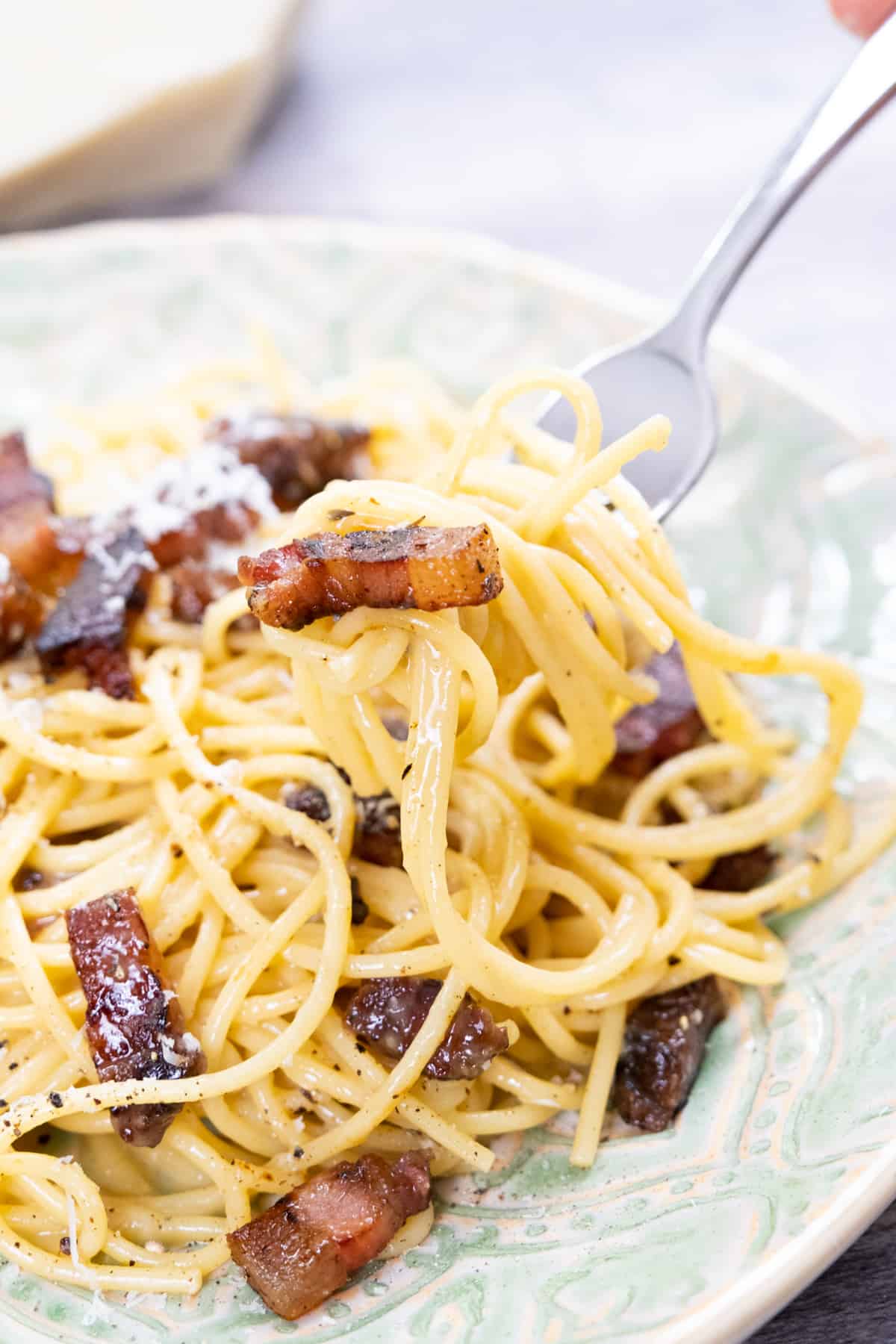 Spaghetti carbonara with guanciale being picked up with a fork.