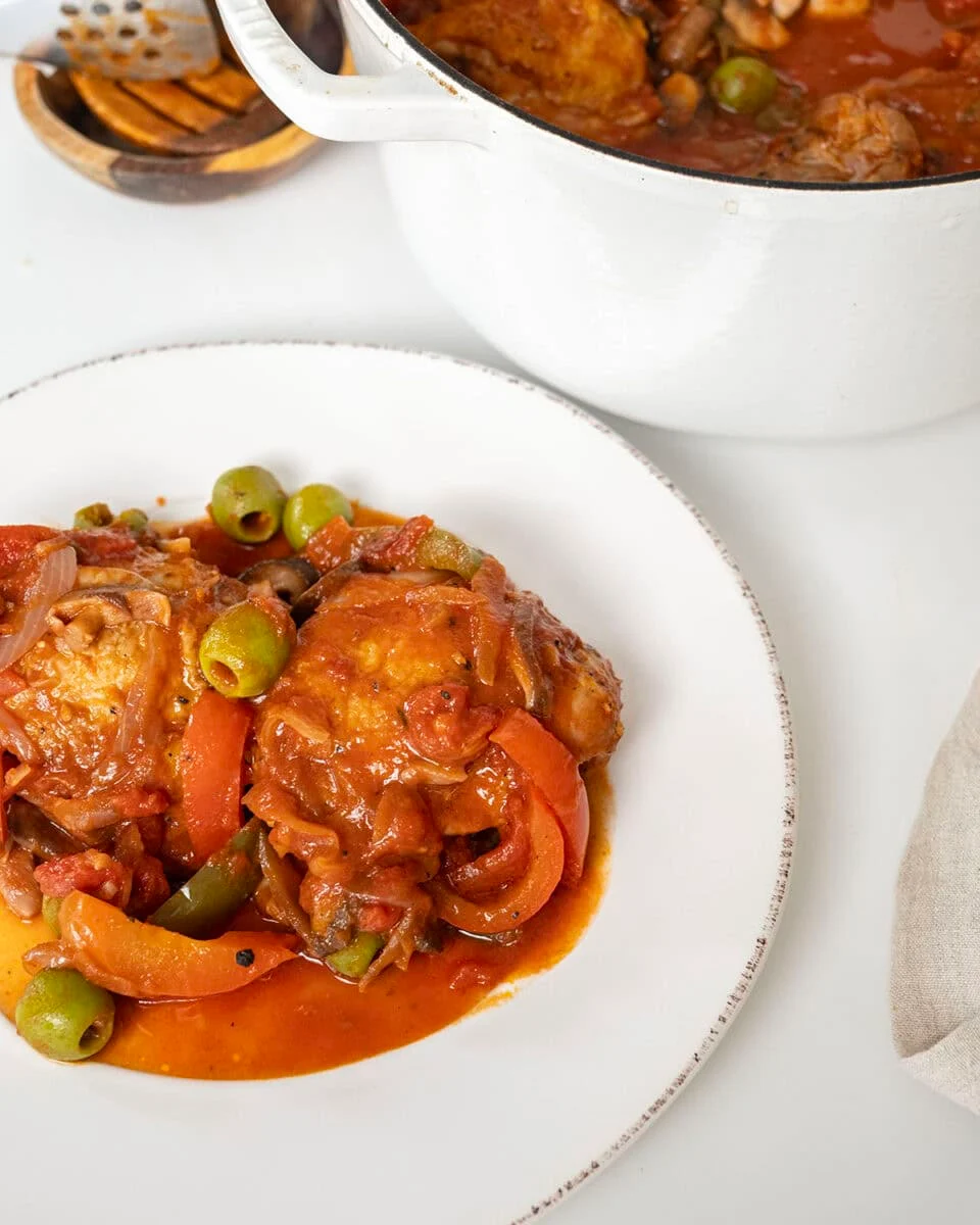 Finished chicken cacciatore on a plate and the remaining in a dutch oven.