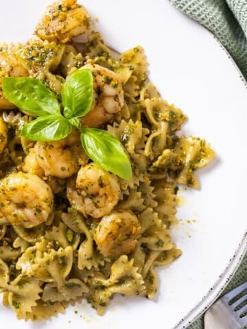 Shrimp over pesto pasta garnished with basil.