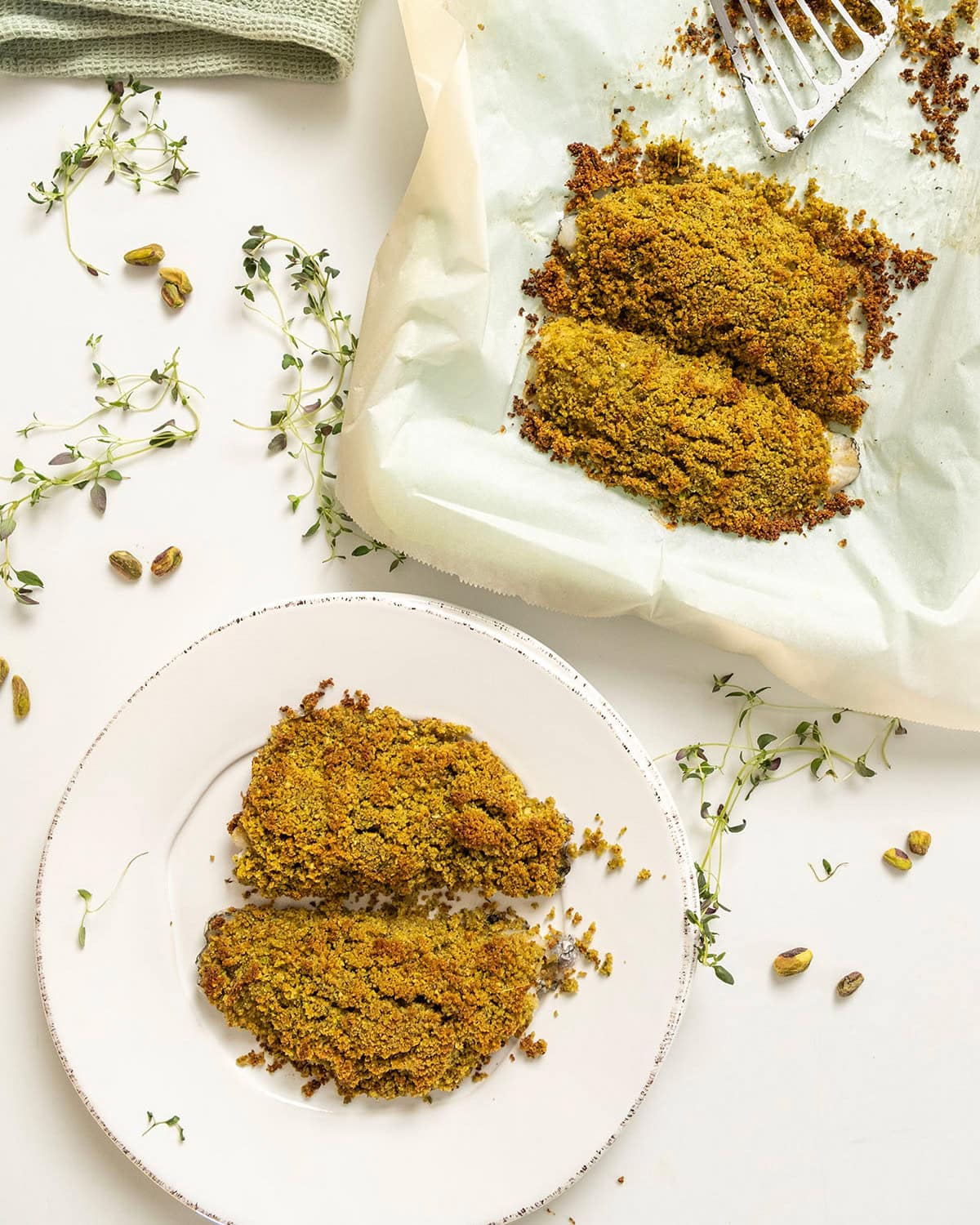 Pistachio crusted sea bass on a plate and baking tray.