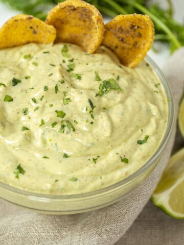 avocado lime crema in a glass bowl with limes and cilantro on side and chips in the crema.