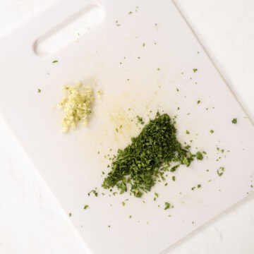 Minced garlic and cilantro on a cutting board.