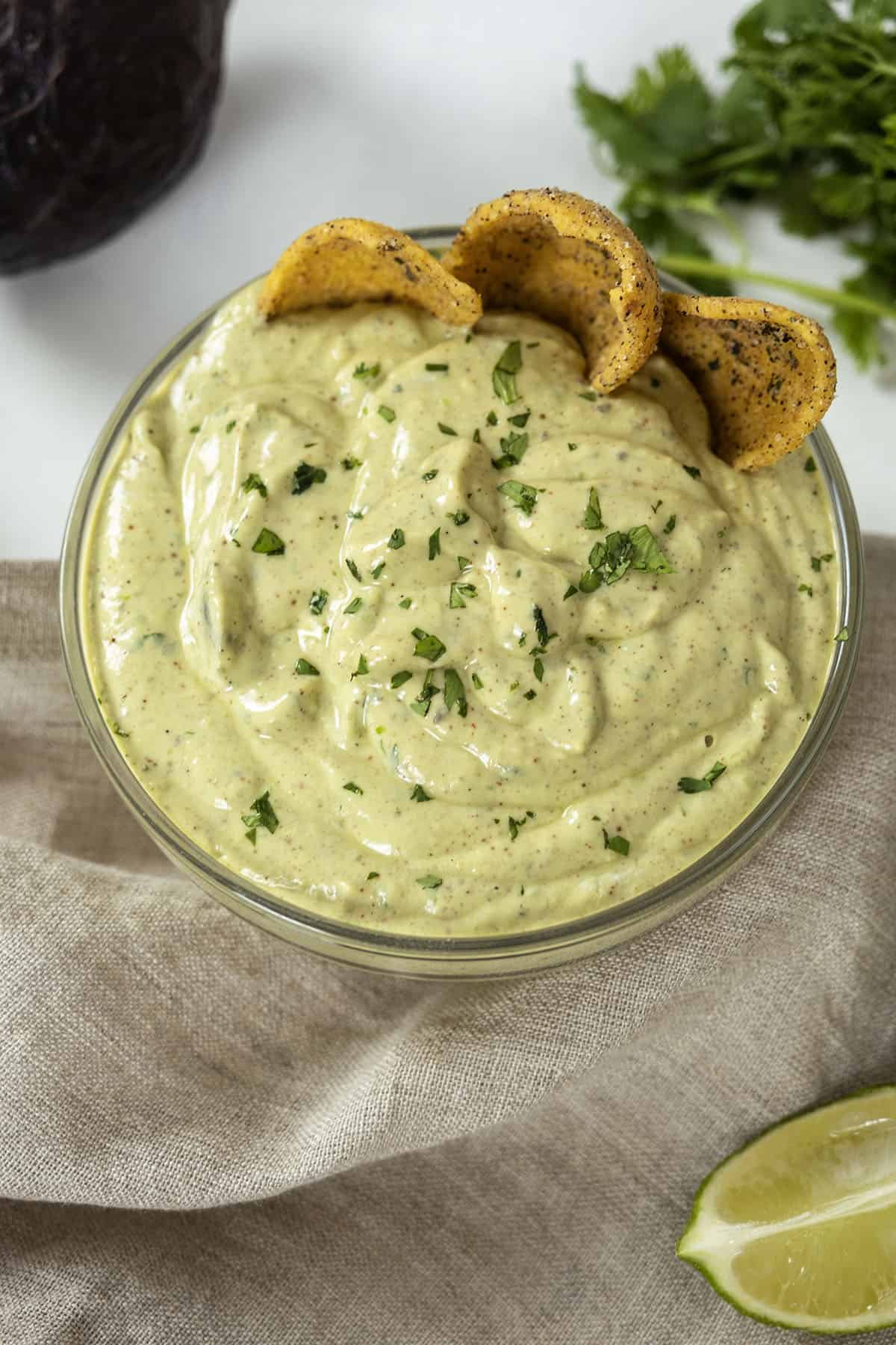 avocado lime crema in a glass bowl with limes and cilantro on side and chips in the crema.