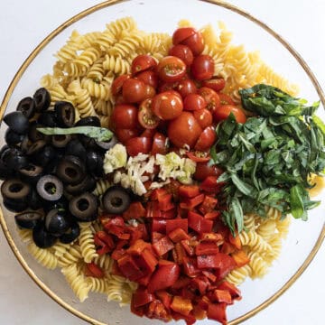 pasta with cherry tomatoes, olives, basil, roasted red peppers, and garlic on top but not mixed in.