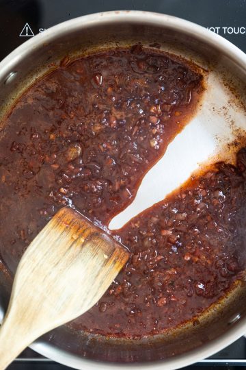 Spoon dragged through red wine reduction with sauce separating due to thickness.