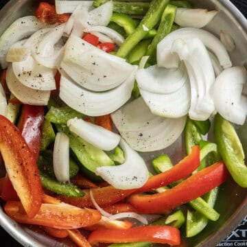 raw peppers and onions sauteing in a frying pan.