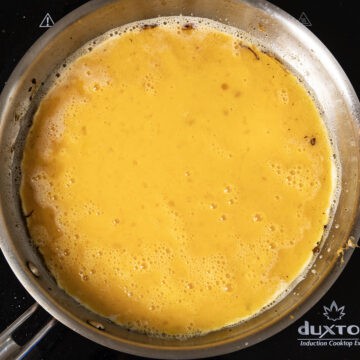 whisked eggs in frying pan with edges beginning to curl up.