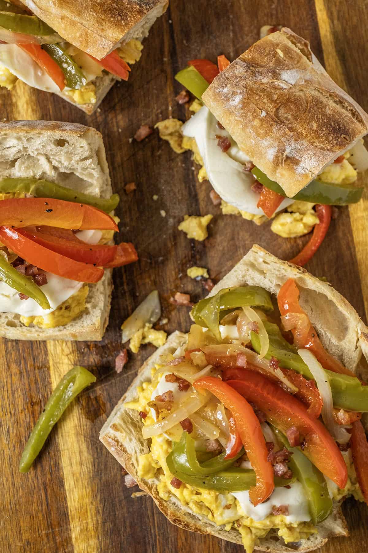 3 Peppers and eggs sandwiches with mozzarella and pancetta on Italian Bread on a cutting board.