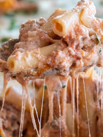Cheesy pull of baked ziti on a spoon being scooped from the baking dish