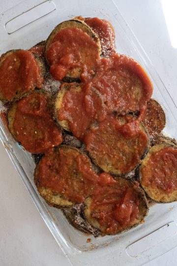 Layering eggplant with sauce in a baking dish.